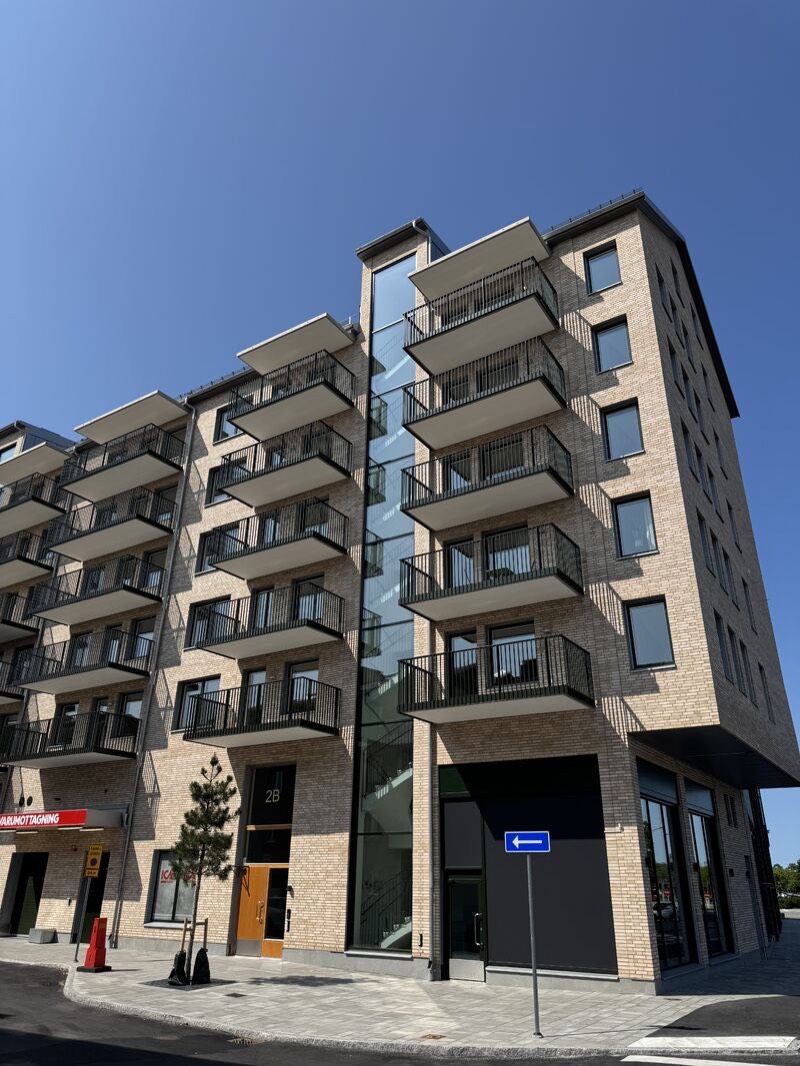 Hörn i ljust tegel sett nedifrån, med balkonger på båda sidor om ett glasat trapphus