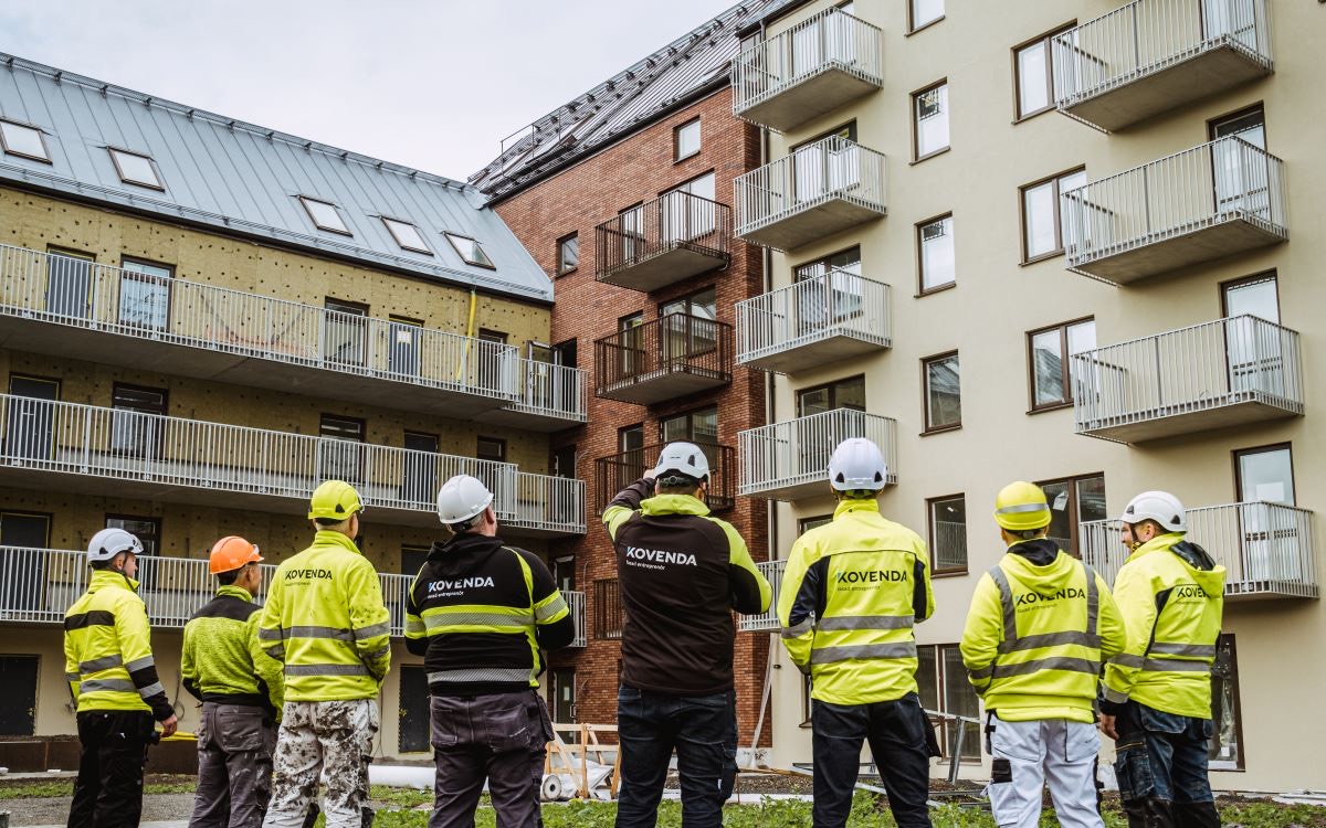 Kovendas hantverkare i varselkläder framför ett nybyggt bostadshus