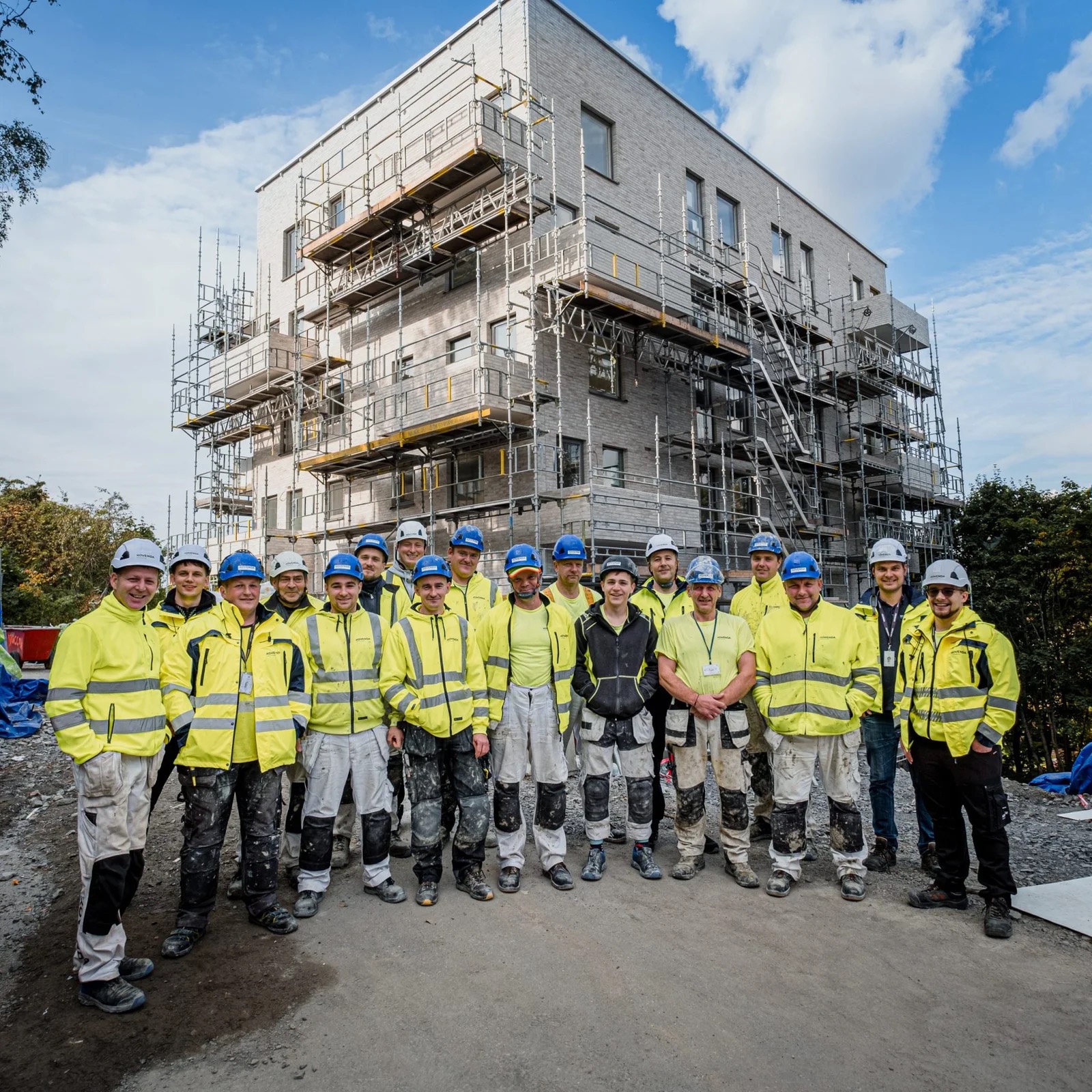 Kovendas hantverkare samlade framför en fasad med ställning