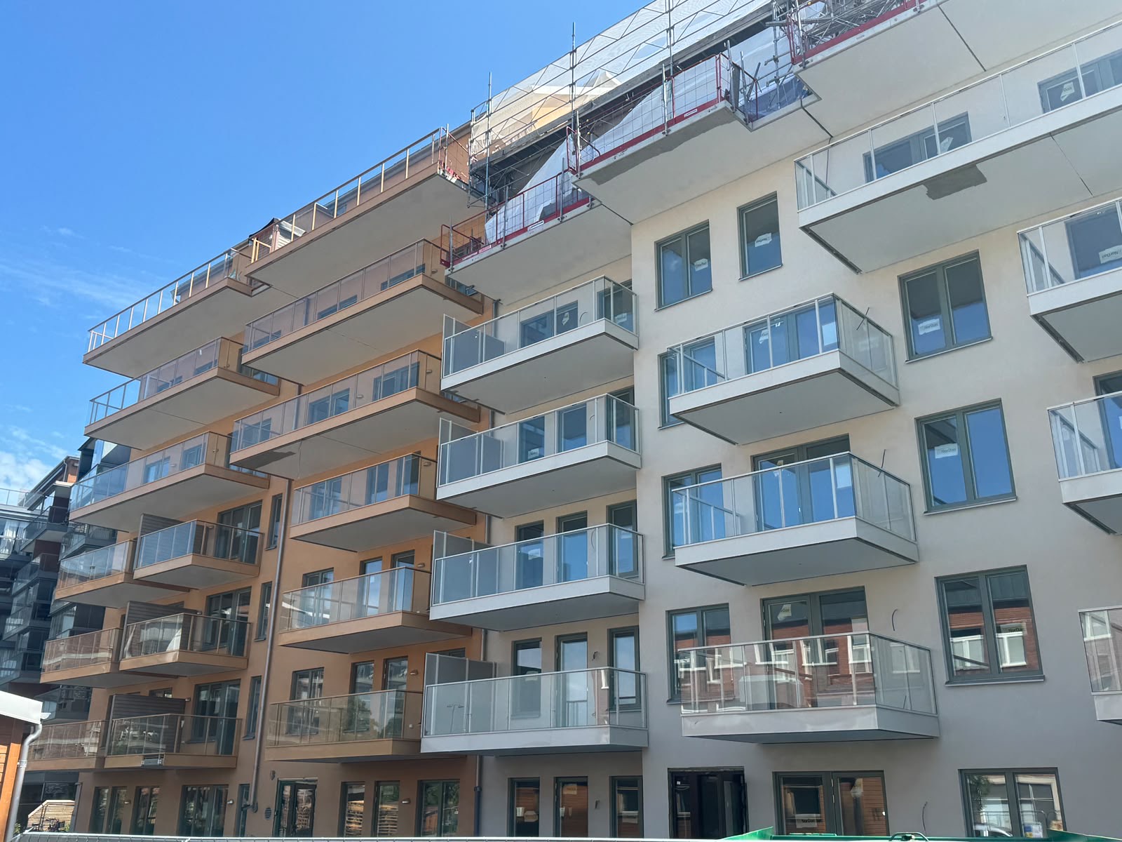 Flerbostadshus med putsad fasad i ljus och orange kulör och inglasade balkonger