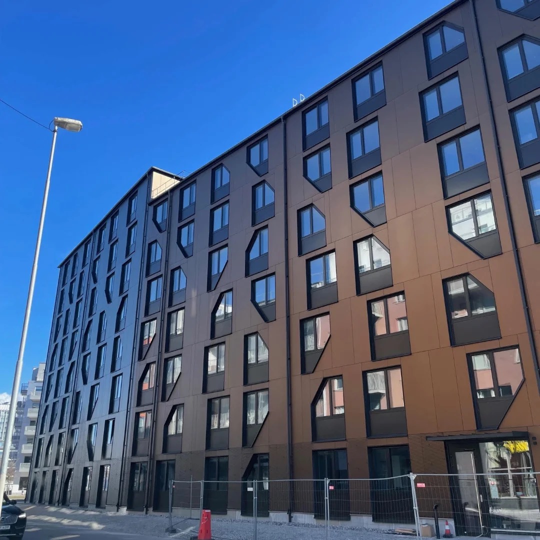 Långfasad på Basecamp Malmö sedd snett från gatan, med fasadskivor som skiftar från mörkt brunt till kopparton