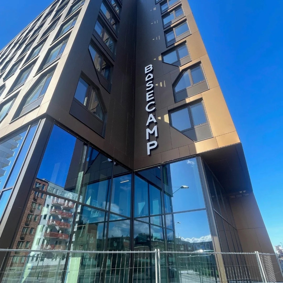 Hörn på Basecamp Malmö sett nedifrån, med skylten Basecamp ovanför en glasad bottenvåning
